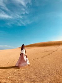 Woman standing on sand dune in desert against sky