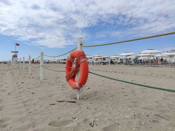 Red lifebuoy hanging on rope at beach against sky