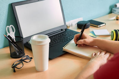 Unrecognizable woman writes on her notebook on a desk in her home