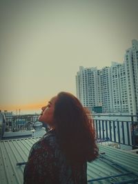 Side view of woman standing by railing against buildings in city