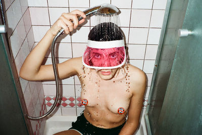 Portrait of topless woman wearing shower cap while taking bath in bathroom