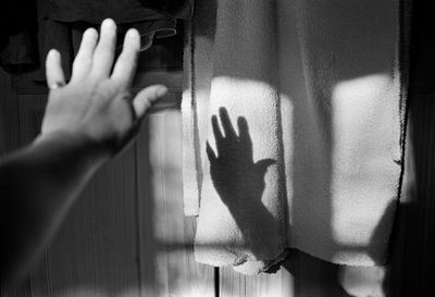 Midsection of person touching shadow on curtain