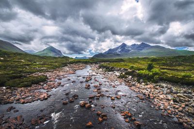 River flowing through rocks against cloudy sky