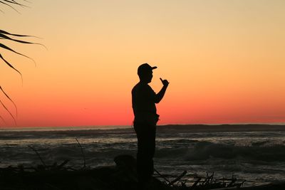 Silhouette man standing on rock against sky during sunset