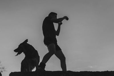 Silhouette man with dog against sky