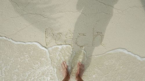 Low section of man standing by text on shore