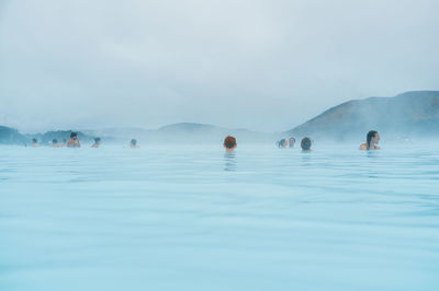 People swimming in lake against sky