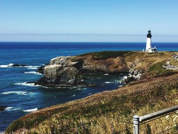 Lighthouse by sea against clear sky