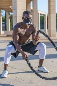 Full length of male athlete exercising with ropes