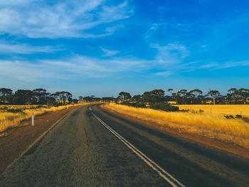 Empty road amidst field against sky