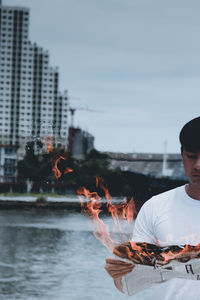 Man holding burning paper against lake and sky