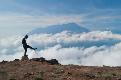 Side view of hiker standing on one leg on mountain peak against sky