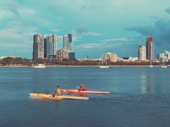 People in river by cityscape against sky