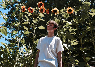 Portrait of young man standing against plants and sunflowers