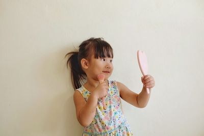 Cute girl applying make-up while looking at mirror against wall