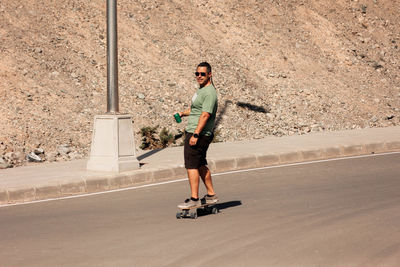 A man playing figure skating on a rural road in the sun on a bright day, play surf skate