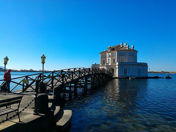 Built structure by sea against clear blue sky