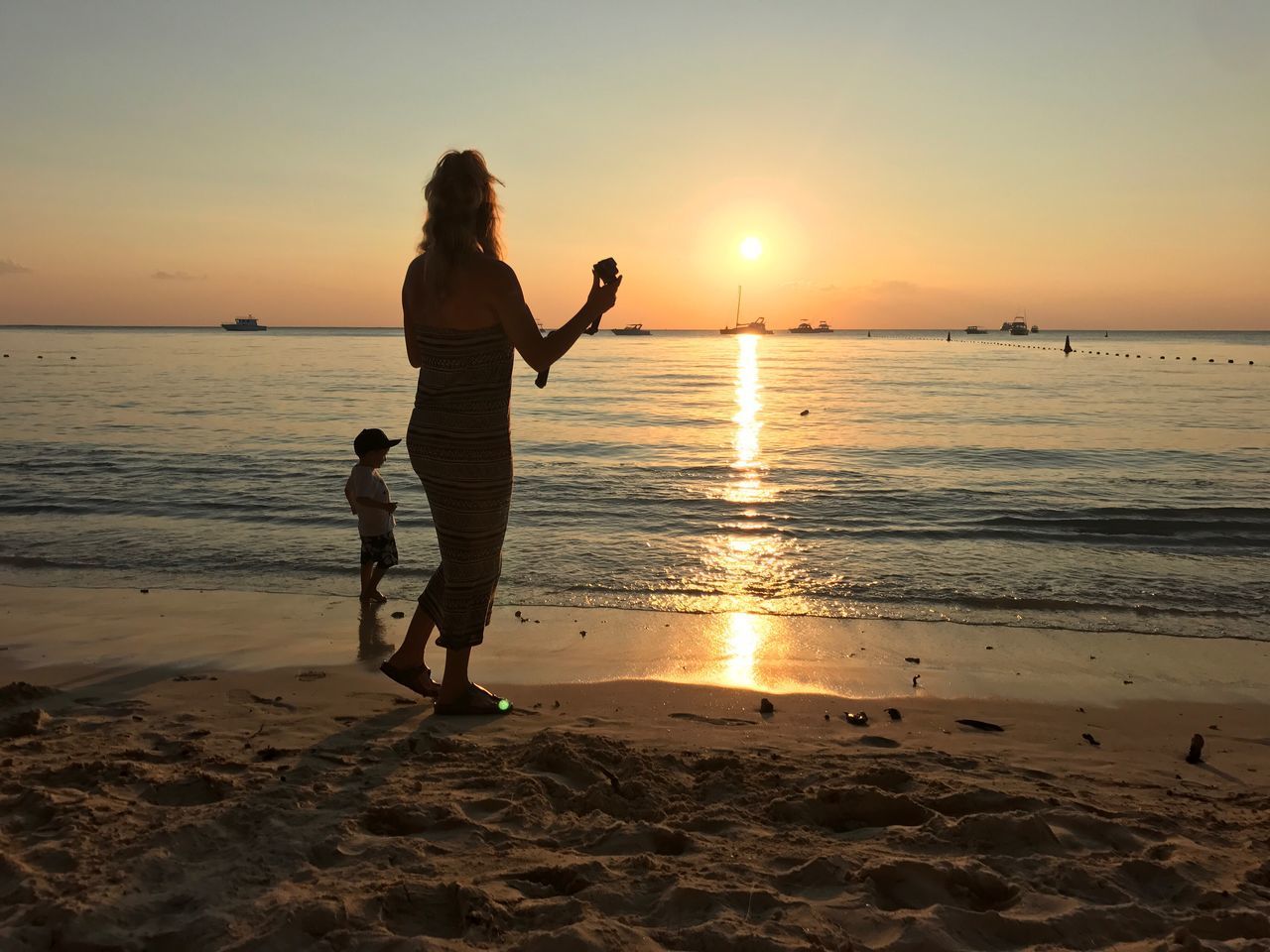 sunset, beach, sand, vacations, sea, real people, nature, two people, shore, scenics, leisure activity, beauty in nature, full length, water, sun, standing, reflection, silhouette, tourism, sky, enjoyment, lifestyles, outdoors, horizon over water, tranquility, women, togetherness, men, wave, people