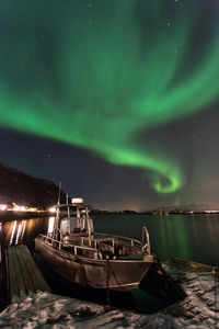 Boat moored at beach against aurora borealis at night