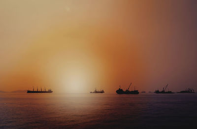 Silhouette boats in sea against sky during sunset