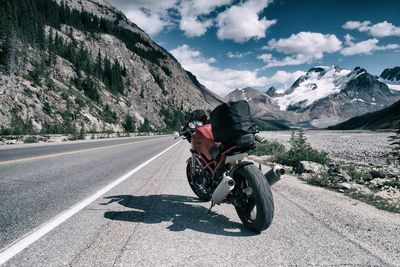 Rear view of man riding motorcycle on road against rocky mountains