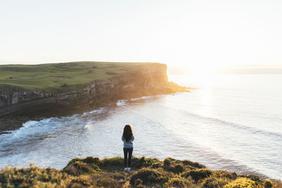 Woman standing at coast looking at sunset over sea