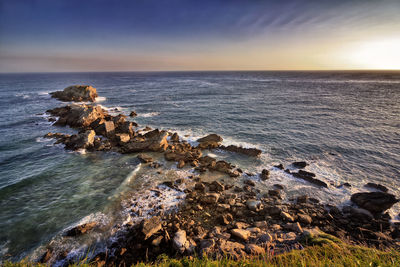 Scenic view of sea by rocks against sky during sunset