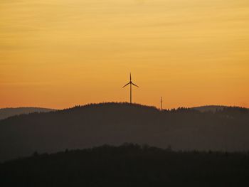 Silhouette wind turbines on land against sky during sunset