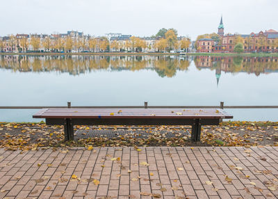 Empty bench by river against buildings in city