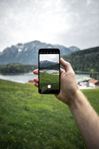 Hand holding smart phone against cloudy sky