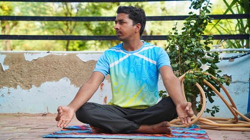 Full of joy young indian man wearing sports clothes blue shirt and black tights in lotus position