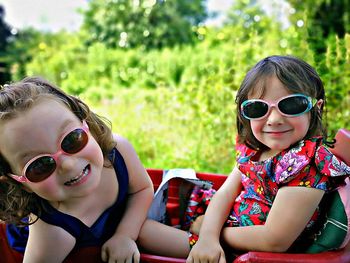 Portrait of smiling girls wearing sunglasses while sitting outdoors