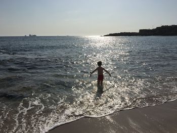 Rear view of woman standing on beach against sky