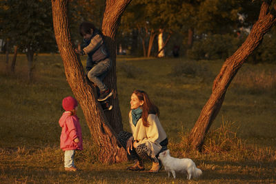 Mother with two children and white dog walking in autumn park at sunset. 