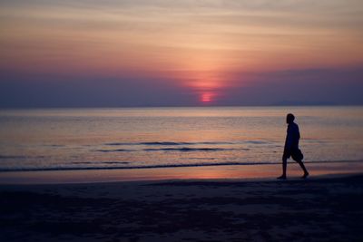 Silhouette man walking on beach against sky during sunset