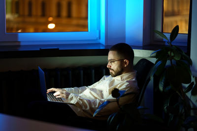 Tired programmer in dark office work on laptop. workaholic businessman typing on computer at night