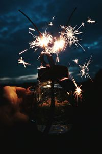 Close-up of hand holding sparklers in jar against sky at night