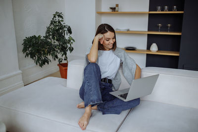 Young woman using mobile phone while sitting on sofa at home