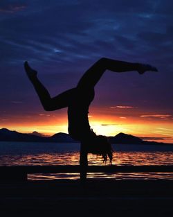 Silhouette person with umbrella on shore against sky during sunset