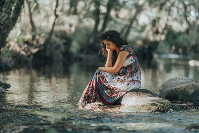 Young woman sitting on rock by lake