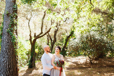 Happy friends standing by tree against plants