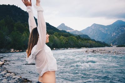 Side view of woman standing by sea against mountain