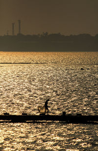 Silhouette man by sea against clear sky during sunset