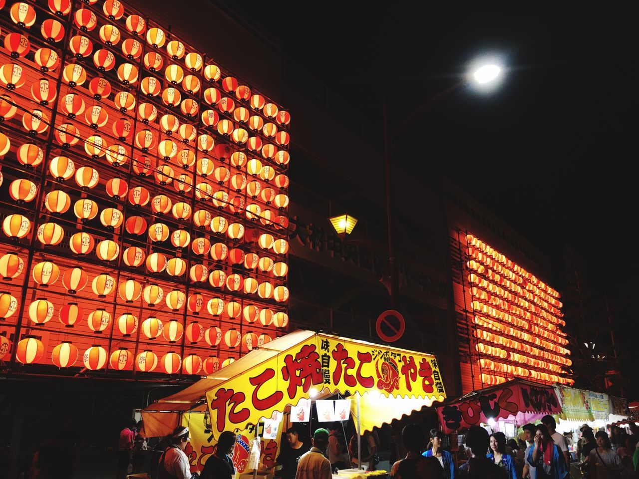 illuminated, real people, group of people, crowd, large group of people, night, lighting equipment, men, built structure, lifestyles, women, architecture, leisure activity, building exterior, adult, city, lantern, hanging, low angle view, outdoors, paper lantern, ceiling