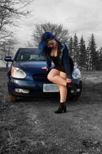Portrait of young woman standing on car against sky