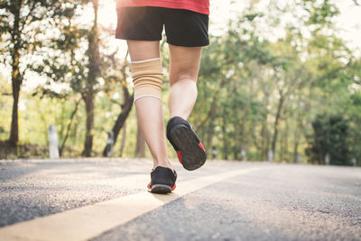 Low section of woman walking on road against trees