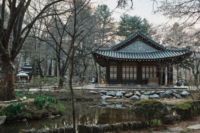 House and trees by lake against sky