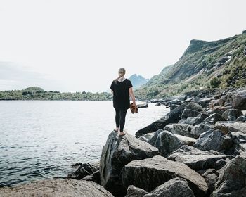 Full length of young woman standing on rock against sky