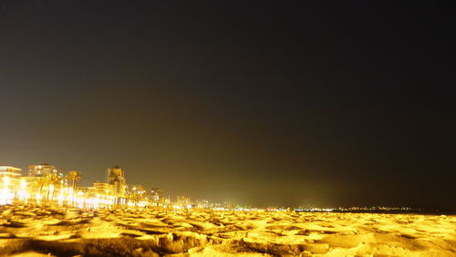 Illuminated cityscape by shiny sandy beach against sky at night