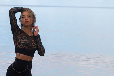 Young woman standing at beach against sky